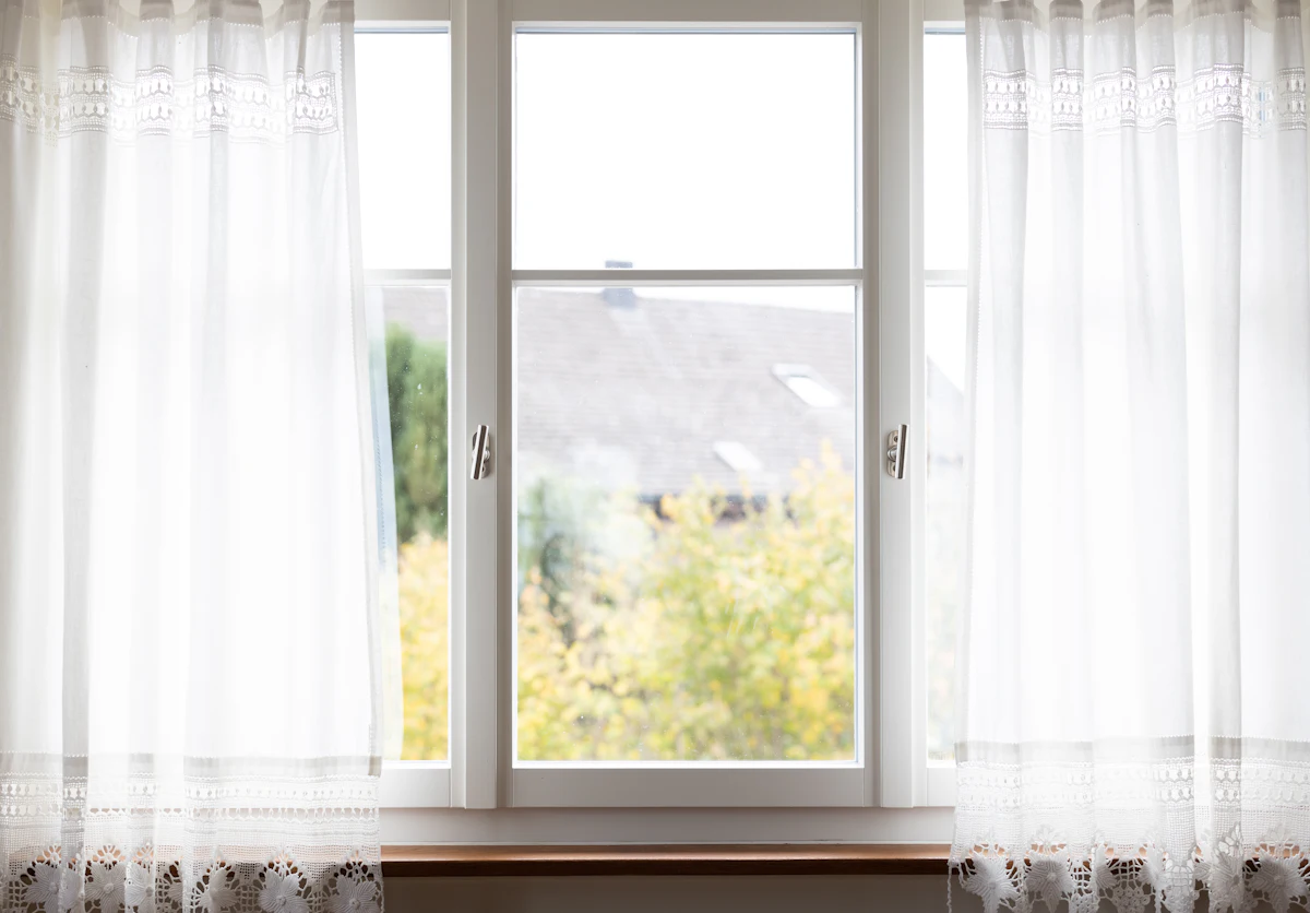 White window frame and sill with sheer curtains, looking out to trees