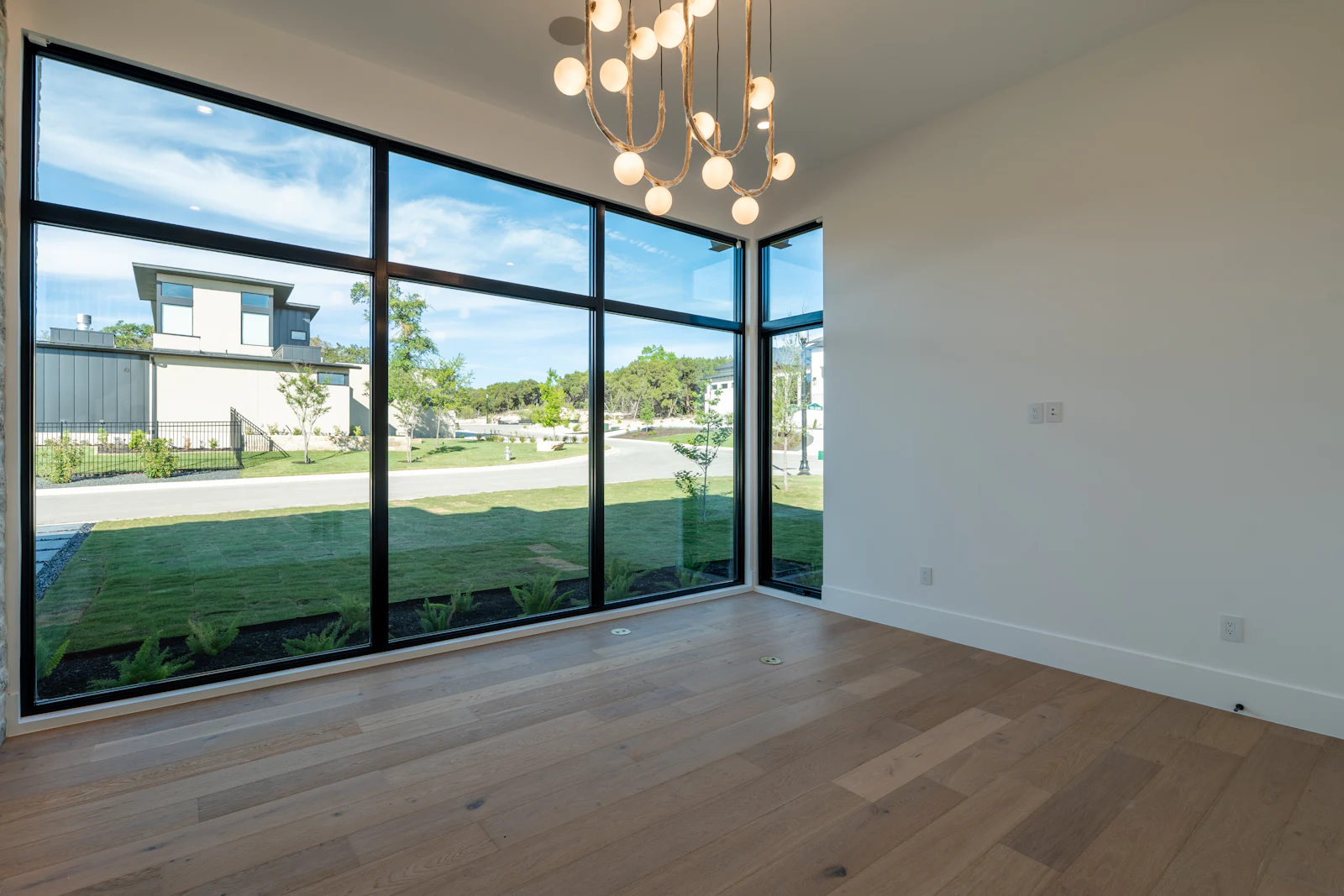 Bright, empty living room with floor-to-ceiling black-framed windows looking out onto a sunny residential street